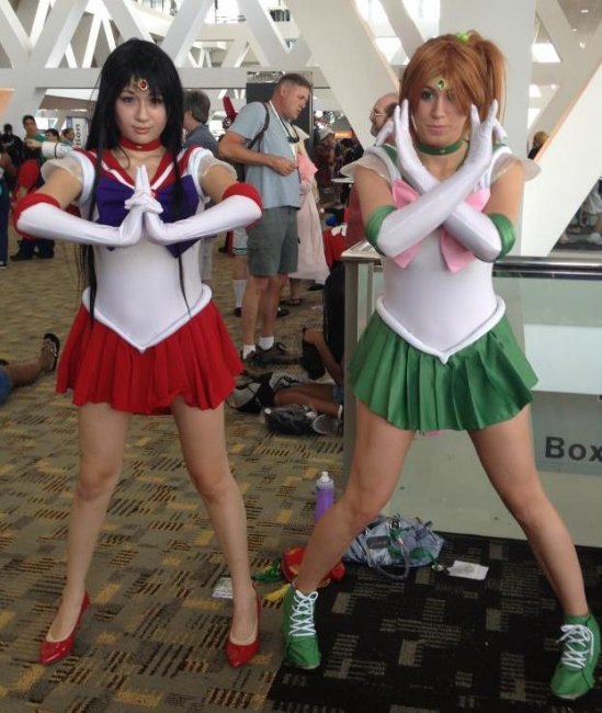 Two costumed young women --- one in a red mini and red pumps , the other in a green mini and green boots --- prepare for action at the anime con. 