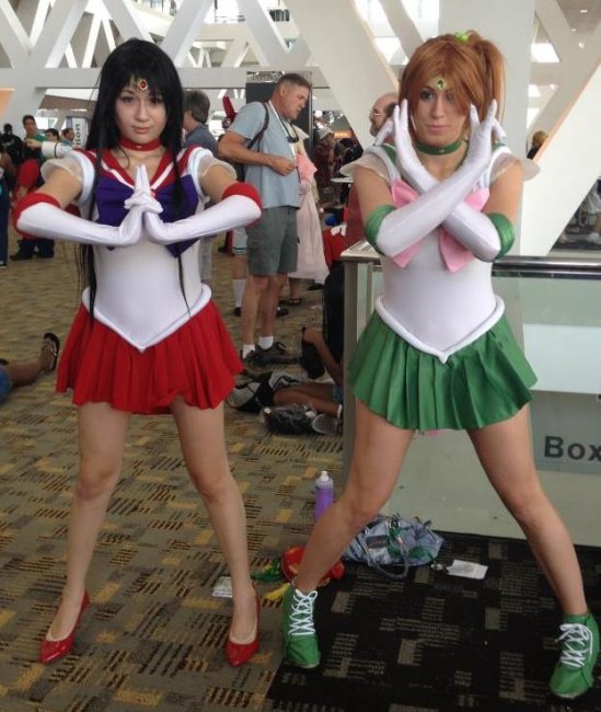Two costumed young women --- one in a red mini and red pumps , the other in a green mini and green boots --- prepare for action at the anime con. Two costumed young women --- one in a red mini and red pumps , the other in a green mini and green boots --- prepare for action at the anime con.