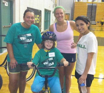 Lose the Training Wheels Camp at Huntington High teaches individuals with disabilities to ride two-wheel bicycles Marshall staff member Megan Archer (left), stands with COHP student Amy Bowen (center), and camp volunteer Brianna (right) as they help 10-year- old Sarah Brown learn to ride a bike during the 2013 Lose the Training Wheels Camp